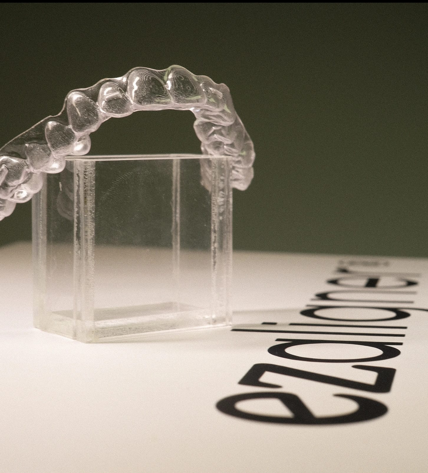 Alinhador dental transparente posicionado sobre caixa e papel com logo ezaligner