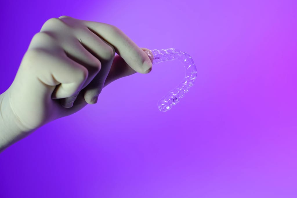 Mão segurando um alinhador dental transparente sobre fundo roxo